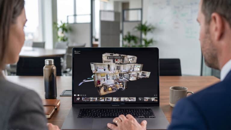 A professional commercial estate agent and property surveyor collaborating and viewing a 3D Dollhouse view of a property virtual tour on a laptop.